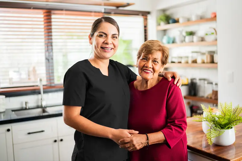 A woman who learned how to become a caregiver smiles as she places her arm around an older woman.