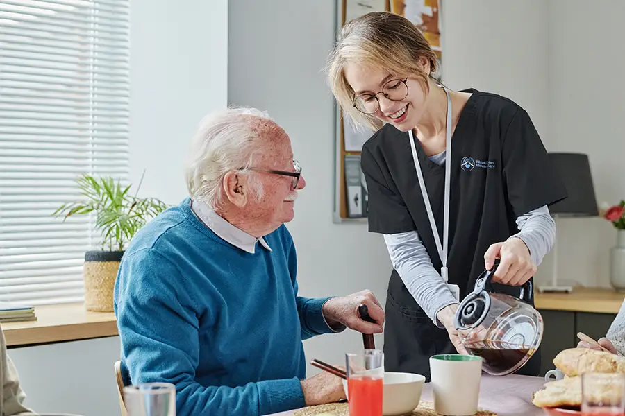 Young caregiver pouring coffee for senior man
